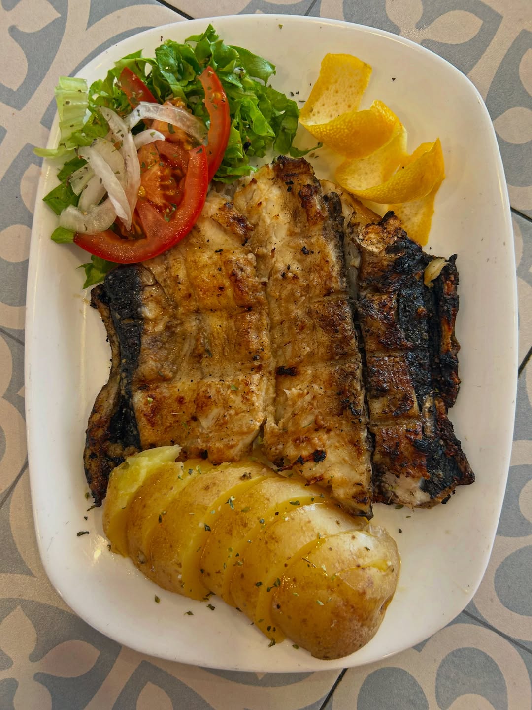 Peixe grelhado com batata cozida e salada, sobre prato branco